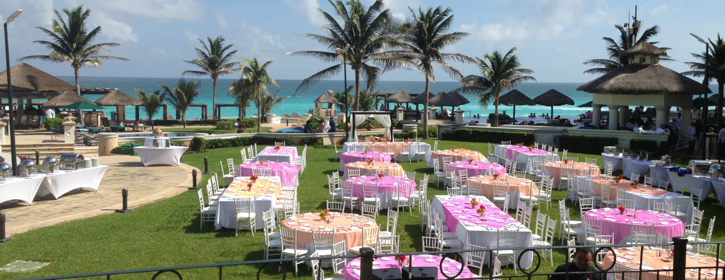 Reception tables set on a lawn beside a turquoise ocean
