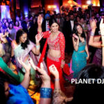 A woman in a red outfit dances energetically surrounded by others in colorful attire at a lively event.